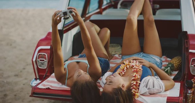 Two happy smiling young women taking selfies with camera in a vintage car at the beach, local hawaii beach lifestyle, summer island fun at the beach
