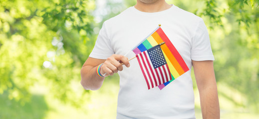 lgbt, same-sex relationships and homosexual concept - close up of man wearing gay pride rainbow awareness wristband and holding american flag over green natural background