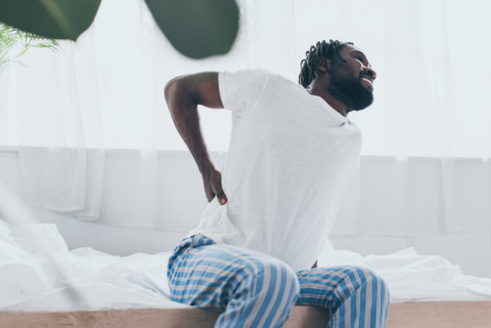 Selective Focus Of Young African American Man Suffering From Back Pain In Bedroom