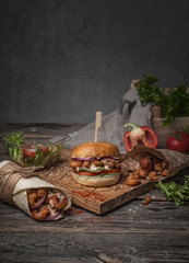 food photography of still life with fast food burger, salad, shrimp and roll side view on a wooden board in a rustic style on gray background close up