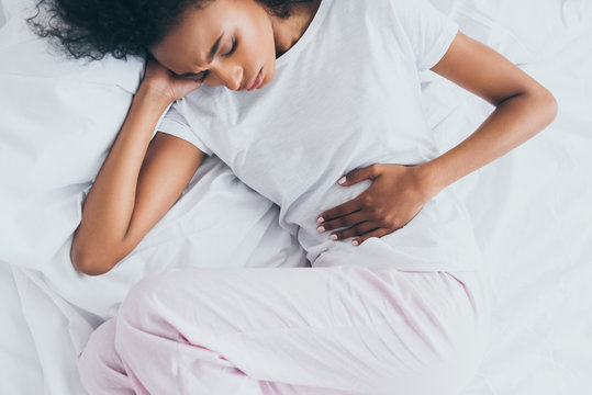 pretty african american woman suffering from stomach pain while lying in bed