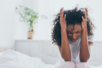 exhausted african american woman suffering from headache in bedroom