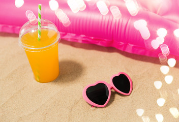 vacation and summer holidays concept - pink sunglasses, orange juice and swimming mattress on beach sand