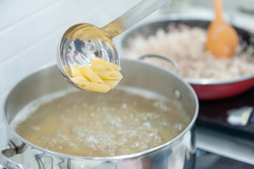 Close-up view, young woman preparing penne pasta boiling water in the pot