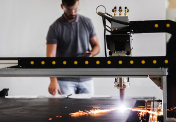 Young engineer setup plasma cutter for work in metalwork workshop.