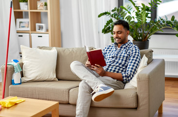 household and people concept - indian man reading book and resting after home cleaning