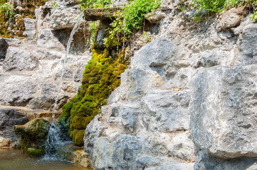 rocky cliff overgrown with green moss. A small waterfall or stream of cold water. Summer