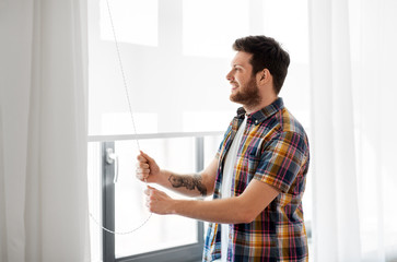 people concept - young man opening or closing roller blind on window at home