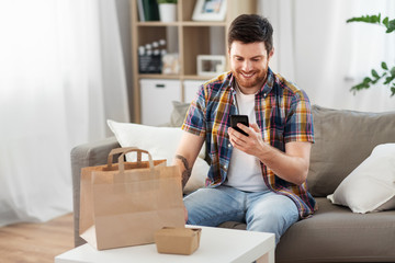 technology, consumption and people concept - smiling man using smartphone for food delivery at home