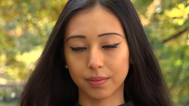 A young Asian woman looks seriously at the camera in a park - face closeup