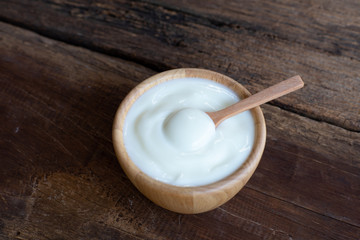 Natural homemade plain organic yogurt in wooden bowl and wood spoon on wood texture background