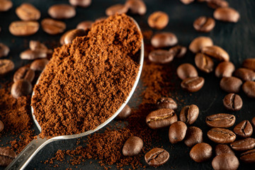 A metal spoon with ground coffee lies on a slate tray, on which coffee seeds are spread out.