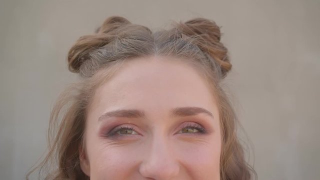 Closeup shoot of young cute caucasian female face with hair buns with eyes looking at camera with urban city on the background