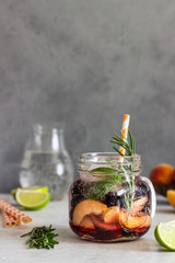 Homemade apricot and black currant lemonade in glass with fresh apricot, rosemary, mint and lime over light grey stone table. Refreshing summer drink. Cocktail bar background concept. Copy space.
