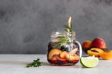 Homemade apricot and black currant lemonade in glass with fresh apricot, rosemary, mint and lime over light grey stone table. Refreshing summer drink. Cocktail bar background concept. Copy space.