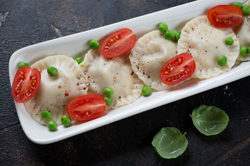 Ravioli served with cherry tomatoes and green peas, close-up, selective focus