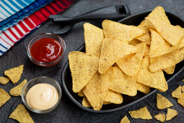 Cast-iron serving tray with nachos chips and dipping sauces, studio shot over grey stone background