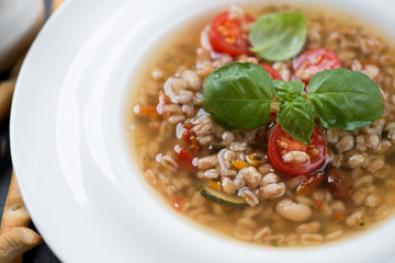 Closeup of a white plate with italian spelt and minestrone soup, selective focus