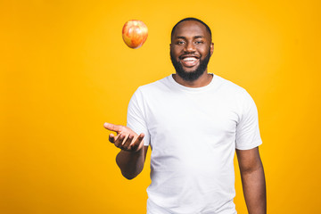 Healthy african american man holding an apple isolated against yellow background.
