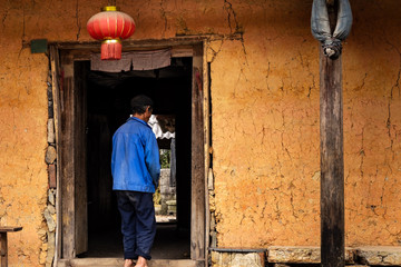 Obraz na płótnie Canvas Unrecognisable hmong farmer seen from the back entering a traditional hmong house with a chinese lantern hanging in Ha Giang Province, Northern Vietnam.