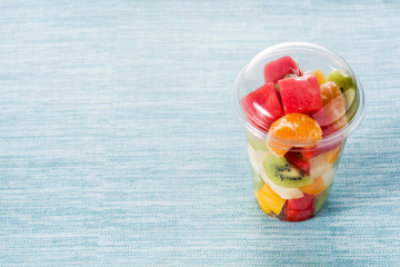 Fresh cut fruit in a plastic cup on blue background