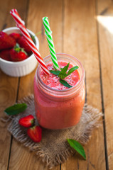 Close-up of strawberry smoothie in a glass jar with fresh mint, on wooden background