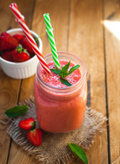Close-up of strawberry smoothie in a glass jar with fresh mint, on wooden background