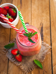 Close-up of strawberry smoothie in a glass jar with fresh mint, on wooden background