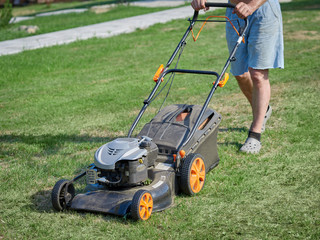 European man is working on the personal plot, he is using lawn mower.