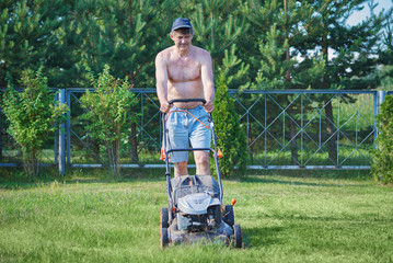 European man is working on the personal plot, he is using lawn mower. © Artem
