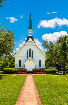 A small white Methodist church down a brick walk under blue skies