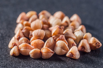 Obraz premium A small pile of buckwheat cereal closeup on a dark background. Macro shooting.