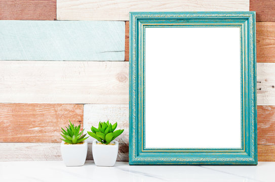 Blank vintage photo frame on wooden wall with cactus plant.