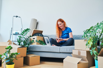 Beautiful smiling young woman sitting in new apartment and using tablet