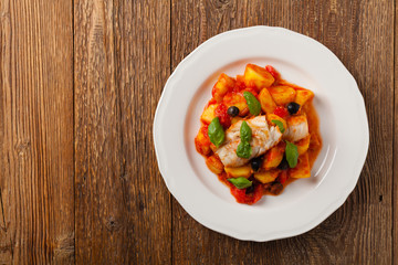 Traditionally prepared cod in Spanish. Served in tomato sauce with boiled potatoes, olivki and basil. Top view.