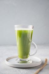 Green matcha tea in latte glass on grey table. Space for text. Close up. Vertical orientation.
