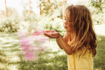 Image of cute blond little girl is playing in the park blowing magical pink dust for an imagination...
