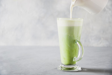 Green matcha tea and pouring milk in latte glass on grey table. Space for text. Close up. Horizontal orientation.