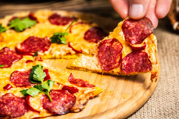 Slices of pizza with cheese and salami in hand on a wooden plate