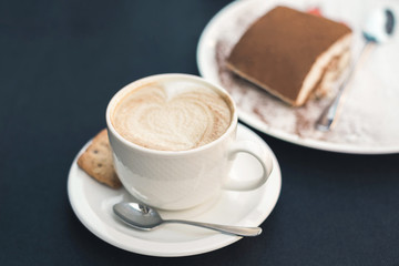 Two cups of coffee and tiramisu on black table background with beautiful latte art heart shaped.