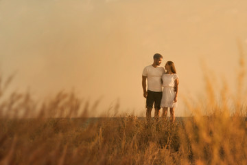 man and woman walking in field at sunset