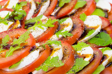 Italian cuisine Caprese Salad close-up. tomatoes mozzarella cheese basil olive oil pepper sauce. Mediterranean Recipe for Fresh Vegetable Salad Organic Vegetarian