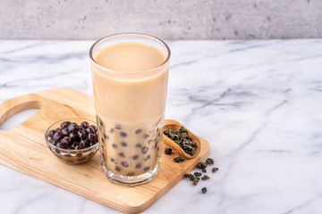 Popular Taiwan drink - Bubble milk tea with tapioca pearl ball in drinking glass on marble white table wooden tray background, close up, copy space