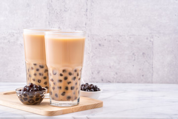 Popular Taiwan drink - Bubble milk tea with tapioca pearl ball in drinking glass on marble white table wooden tray background, close up, copy space