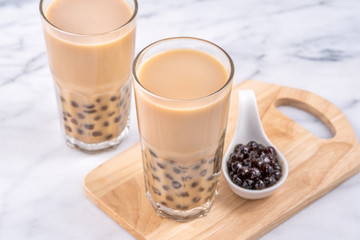 Popular Taiwan drink - Bubble milk tea with tapioca pearl ball in drinking glass on marble white table wooden tray background, close up, copy space