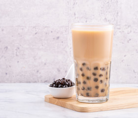 Popular Taiwan drink - Bubble milk tea with tapioca pearl ball in drinking glass on marble white table wooden tray background, close up, copy space