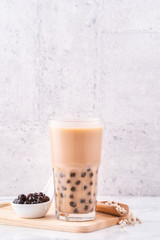 Popular Taiwan drink - Bubble milk tea with tapioca pearl ball in drinking glass on marble white table wooden tray background, close up, copy space
