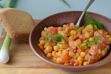 Roasted chickpeas in a clay plate with greens and bread on a wooden board