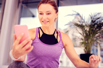 Positive delighted aged woman staring at her gadget