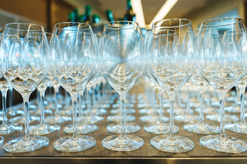Several rows clear, clean glasses for wine and champagne on counter prepared for drinks.
